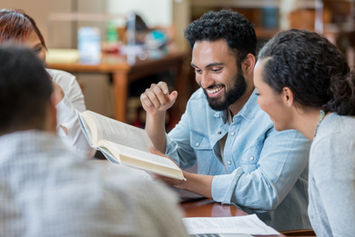 Three smiling individuals gathered around a table, looking at books together.