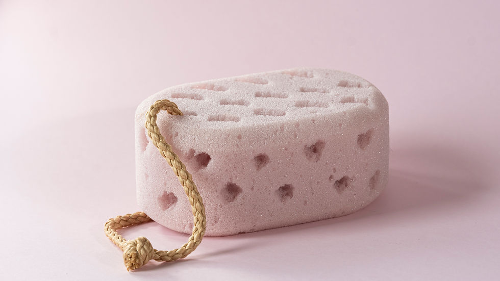 Pink pumice stone with heart patterns and a rope handle on a matching pink background. The scene feels soft and calm.