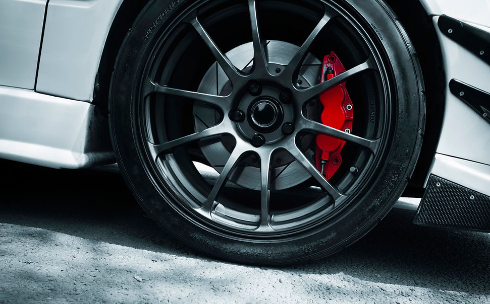 A close-up of a car wheel with a black alloy rim and red brake caliper.