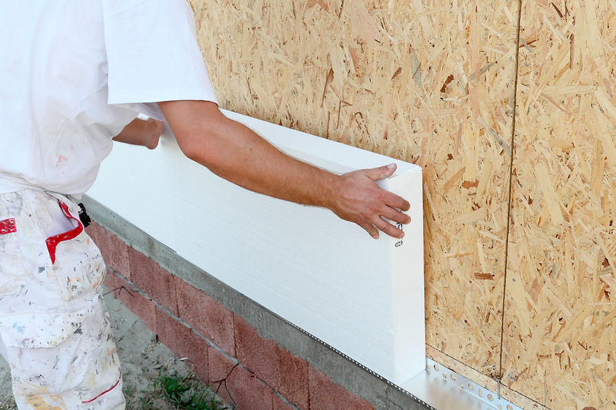 A person installs a white insulation panel on an OSB exterior wall