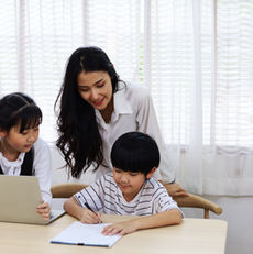 Teacher assisting two students with schoolwork using laptop