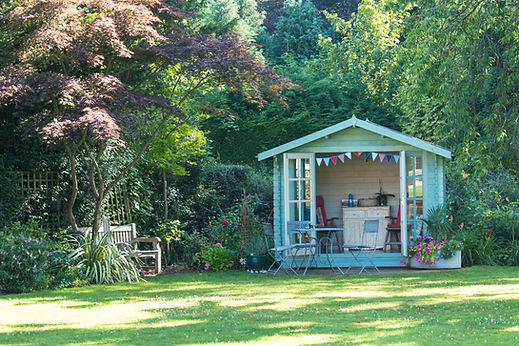 Light blue timber garden room shed surrounded by lush trees and grass