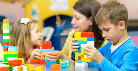 Kids playing with plastic building blocks at pre-school while professional team watches