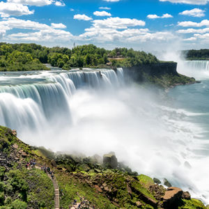 Breathtaking view of Niagara Falls with cascading waters and lush greenery under a picturesque, cloud-dotted sky.