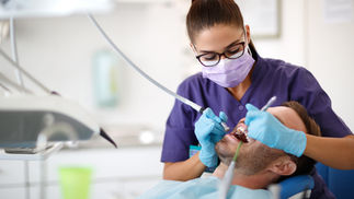 A dental hygienist wearing gloves and a mask performs a professional teeth cleaning on a male patient in a modern dental clinic