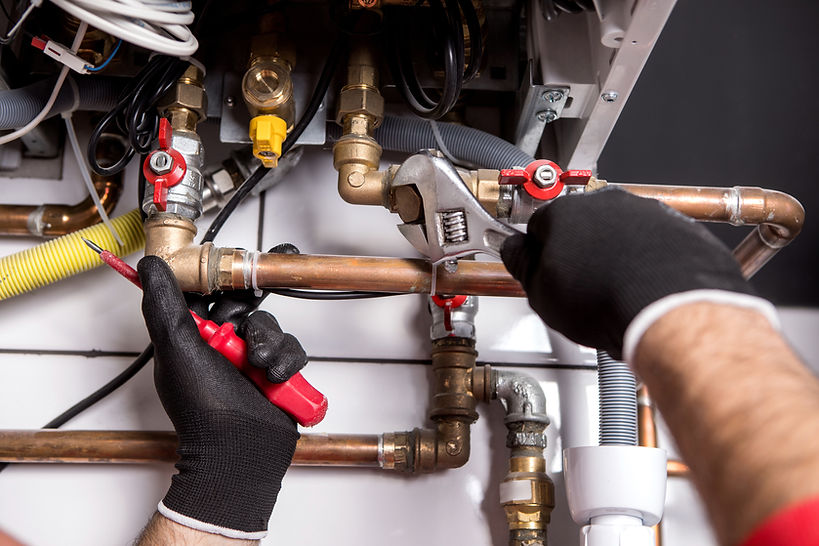 Gloved hands using a wrench and screwdriver on copper plumbing pipes with red valves