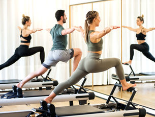 A group of people doing Pilates exercise on reformers