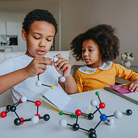 Two young kids play with toy chemistry particles on the table together