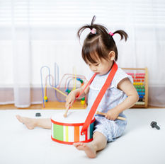 a young toddler sitting on the floor banging on a drum.
