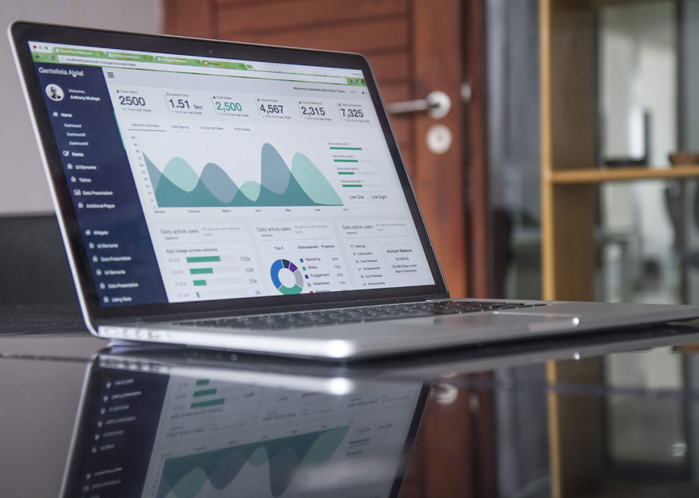 A silver laptop on a table open to a webpage showing a series of graphs, charts, and numbers.