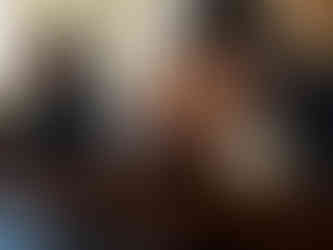 A young Black girl with braids in a black dress stands at a pew in prayer next to an older Black man with braids who has his head bowed to his clasped hands.