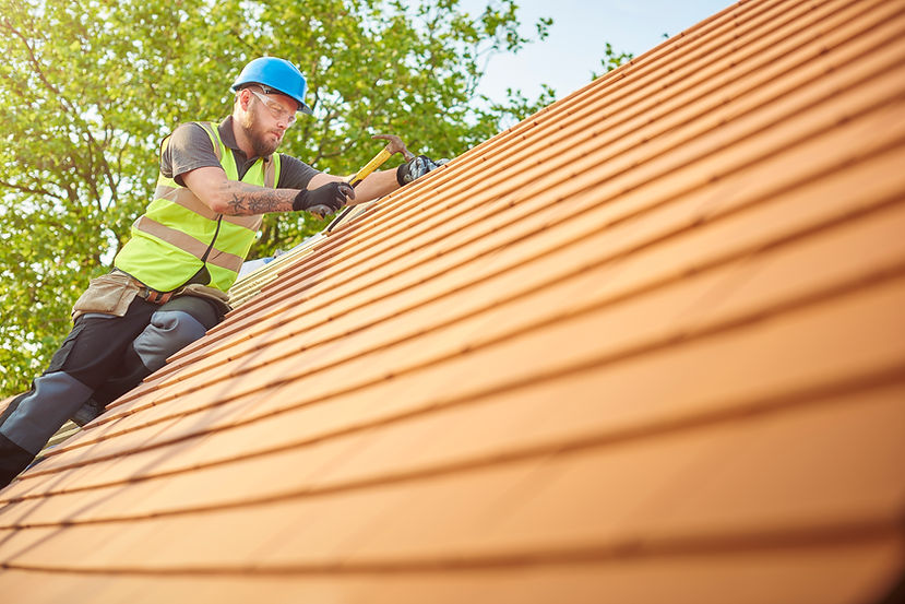 A roofer nails on the roof tiles