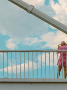 A woman standing thoughtfully on a modern pedestrian bridge during twilight, looking out at the city skyline as warm streetlights begin to glow, capturing a moment of personal reflection and transition.
