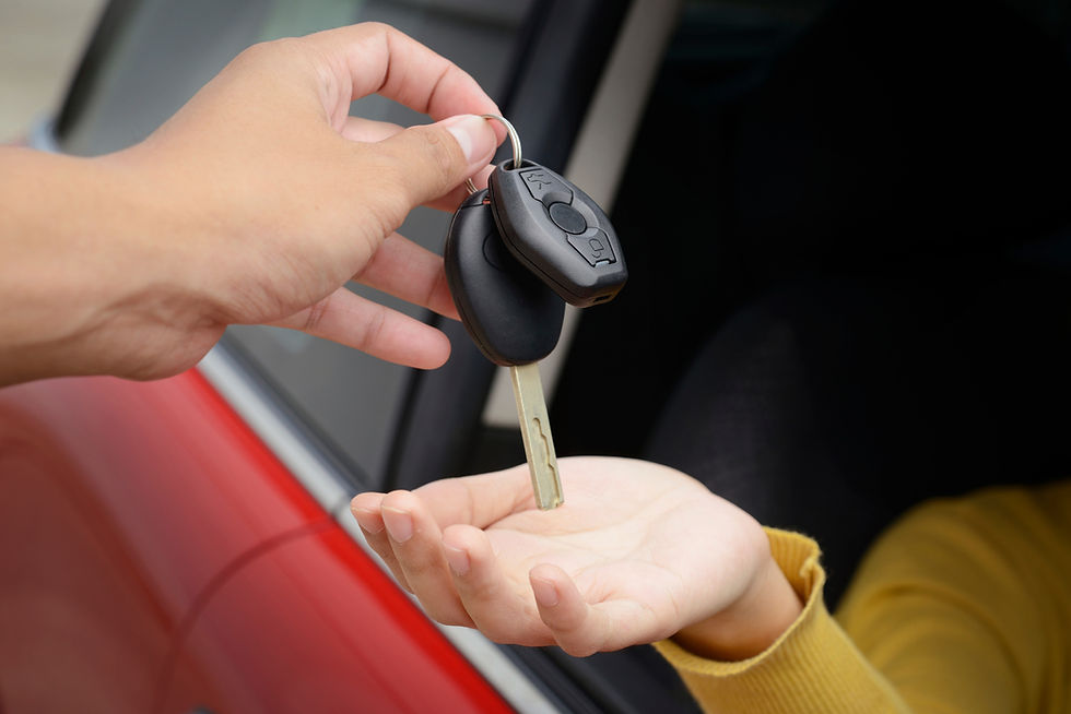 A close-up of a person handing a car key to another person inside a red vehicle
