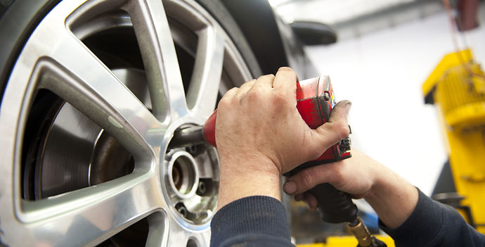 Detail image of mechanic hands with tool, changing tyre of car, with blurred background of