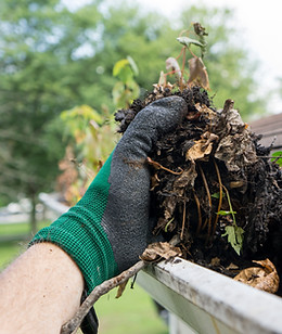 A gloved hand is shown cleaning a gutter clogged with leaves and debris