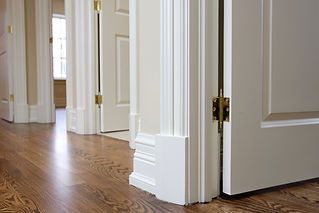 Close up image of the white corner wooden floor and door trim- base board