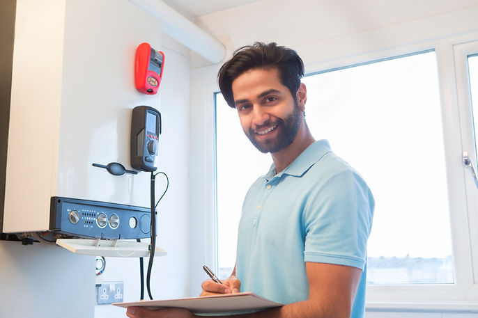 Bearded engineer in a light blue shirt servicing a central heating boiler in a bright indoor setting
