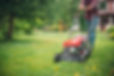 Person mowing a lush green lawn with a red push mower