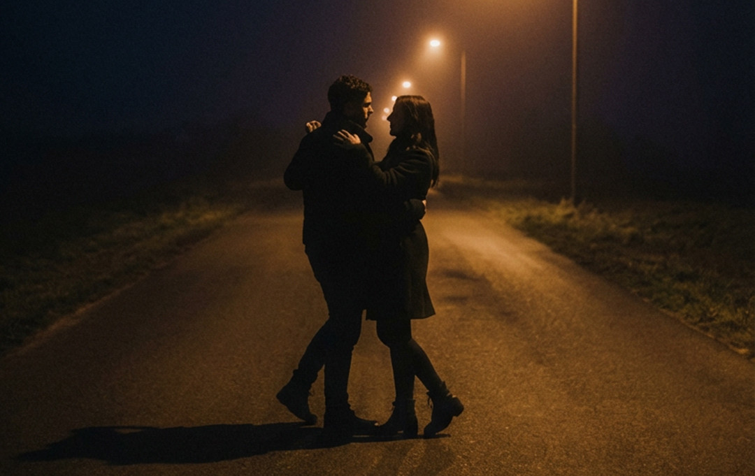 Couple embracing on a foggy empty road at night, lit by warm streetlights, creating a romantic, intimate mood.