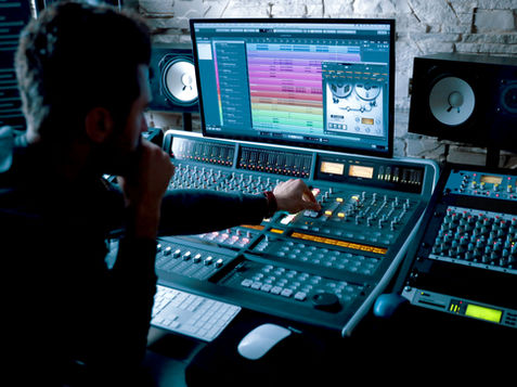 music engineer seated in front of a mixing board and screen