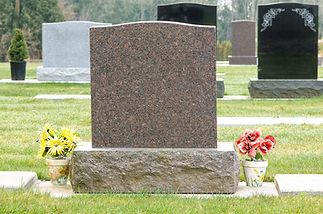 A blank, polished granite tombstone stands on a grassy cemetery
