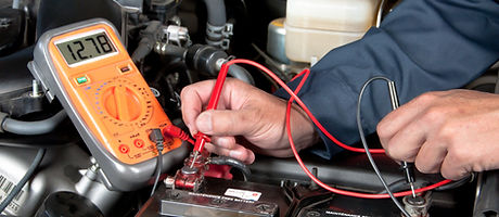 An auto mechanic uses a multimeter voltmeter to check the voltage level in a car battery