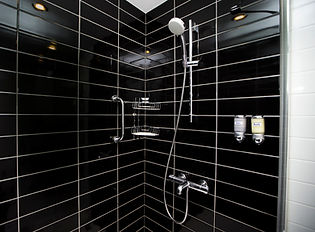 Modern shower with sleek black tiles and white grout, featuring a chrome showerhead, soap dispensers, and shelf