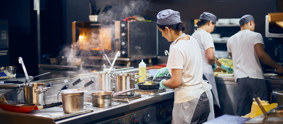 Tres cocineros, con gorros y guantes de chef, trabajan en una cocina moderna.