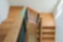 Wooden staircase with a black metal railing viewed from above, leading down to a light wooden floor.