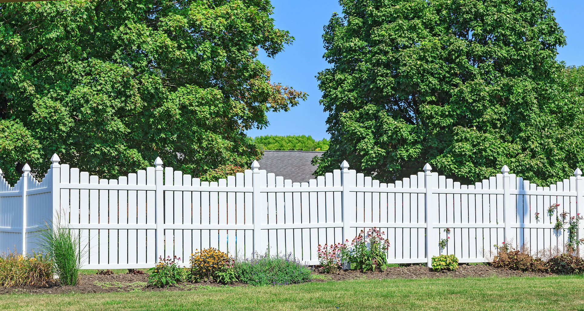 White picket fence in lush garden with flowers and trees