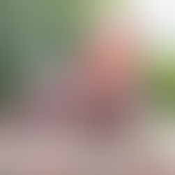 A woman in a floral shirt writes in a notebook at an outdoor table, next to a patterned mug; peaceful greenery in the background.