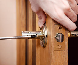 Close-up of a woodworker using a screwdriver to precisely align a new door handle and latch mechanism.