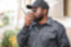 A security guard in a dark uniform and cap speaks into a walkie-talkie