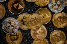 A collection of assorted cryptocurrency coins, including Bitcoin and Ethereum, on a textured black surface, with metallic and golden hues.
