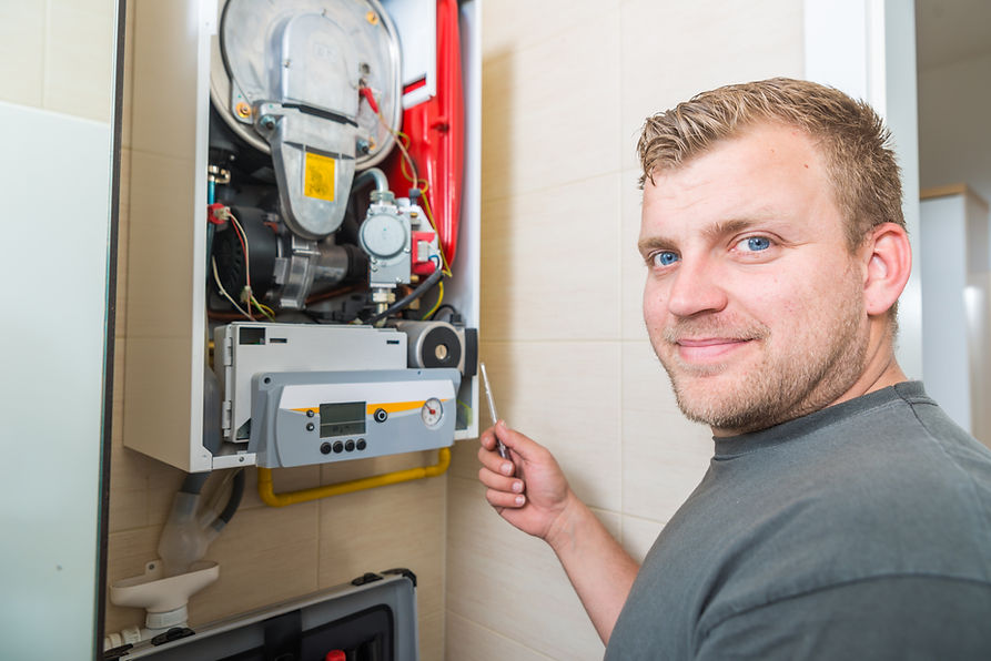 Professional technician in a grey shirt inspecting an open wall-mounted gas furnace with internal red components