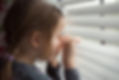Child indoors, looking out through window blinds