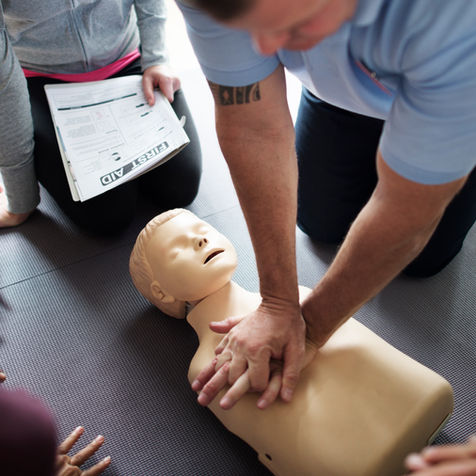 A person performs CPR on a training dummy while others watch