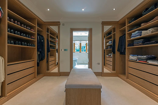 Custom walk-in wardrobe with extensive wooden shoe racks, hanging rails, shelving, and a central bench