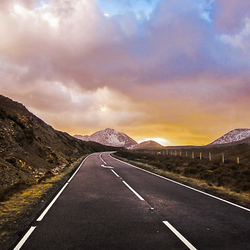 A quiet road leads towards the sunset and snow-capped mountains on the Isle of Skye