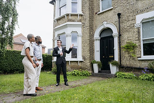 Female estate agent speaking with an older couple on the lawn outside a traditional stone house