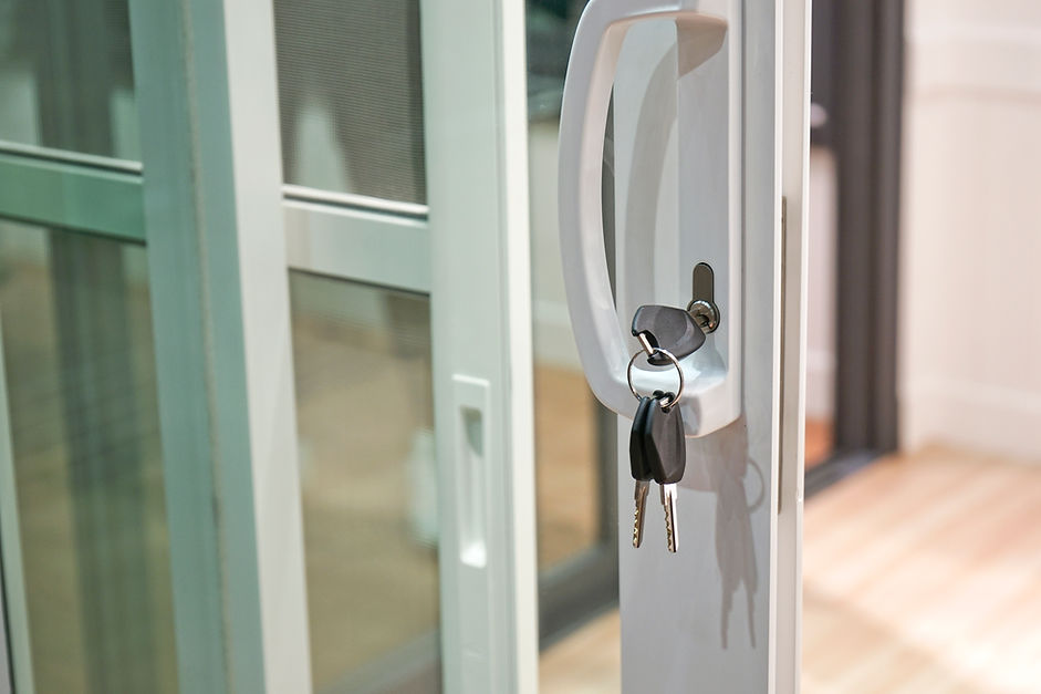 A set of keys hangs from the lock of a white sliding glass door handle.