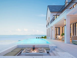 Luxury seaside villa patio with infinity pool, set dining table, and ocean view at dusk, warm lights glowing.
