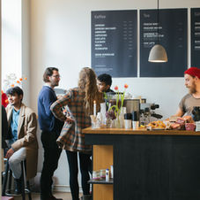 Busy coffee shop with baristas preparing drinks and a display of baked goods.