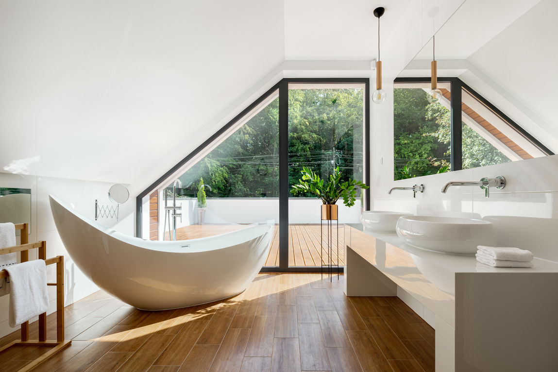 Modern bathroom with freestanding tub, wood floor, large windows.