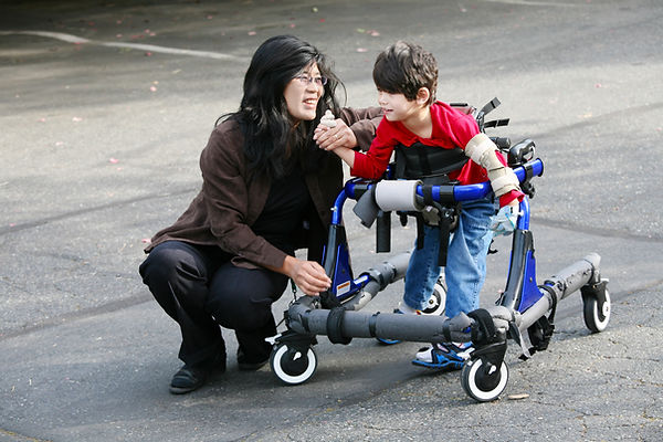Boy using a walking frame supported by carer