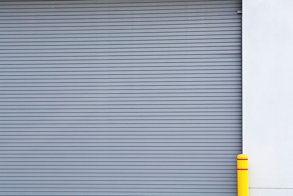 A grey roll-up door with horizontal slats, positioned next to a bright yellow bollard