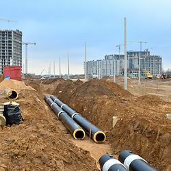 Image of 2 Big Black Industrial Pipes laying on tunnel hole on soil land with blue sky and City Buildings background. Licensed Sealed Engineering Plumbing Blueprint Plans Services Construction Project Available. Book us today! Call us at: (305) 680-3283.