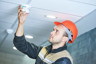 Worker installing a smoke alarm on a suspended ceiling