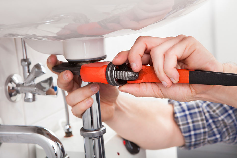 Hands using a red wrench to tighten a pipe under a white sink